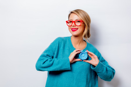 Portrait of a beautiful white smiling woman in blue sweater with little alarm clock on white background, isolated.の写真素材