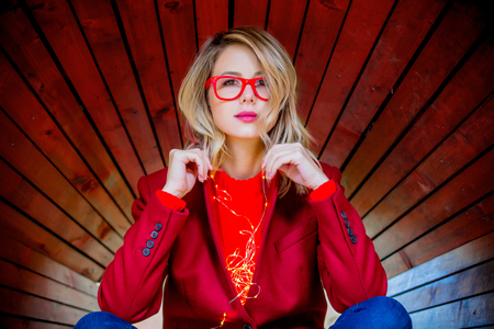 Young style girl in red coat and glasses on wooden background.の写真素材