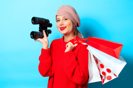 Portrait of a young girl in red sweater with bonocular box and shopping bag on blue backgroundの写真素材