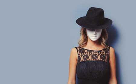 Portrait of a young style girl in black dress and white mask on gray background