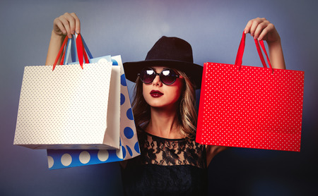 Portrait of a young style girl in black dress and hat with shopping bags on gray background with bokehの写真素材