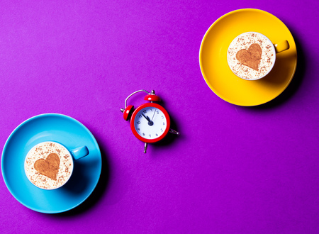 Blue and yellow cups and clock on the purple backgroundの写真素材