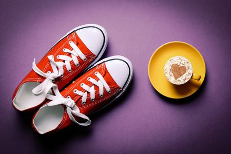Yellow cup of coffee and gumshoes on the purple backgroundの写真素材