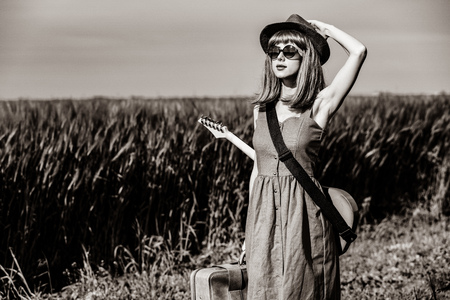 portrait of young beautiful woman with suitcase and electric guitar in the field. Image in black and white color styleの写真素材