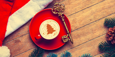 red cup of Cappuccino with key and Christmas hat on wooden table.の写真素材