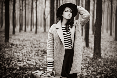 Portrait of a young woman with a suitcase standing in the middle of the forest. Image in black and...