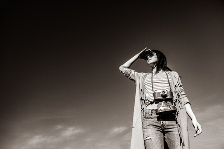 portrait of the beautiful young woman with camera on the sky background. Image in black and white color styleの写真素材