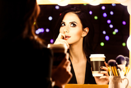 portrait of young beautiful woman with cup of coffee looking in the mirrorの写真素材