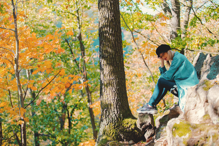 Young girl in blue jeans clothes have a rest in beautiful autumn season forest.の写真素材