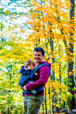 Young father with a child in carrier. located in autumn season parkの写真素材