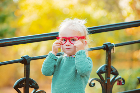 little white blonde girl in red glasses and green sweater in a park. Autumn seasin timeの写真素材