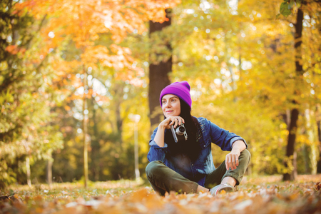 Portrait of a young girl in hat with professional camera on fall season parkの写真素材
