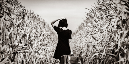photo of the beautiful young woman with suitcase standing in the middle of the fieldの写真素材
