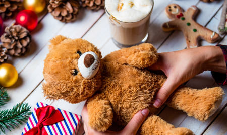 Photo of the female hand holding a teddy bear, cookie and cup of coffee lying on the Christmas...