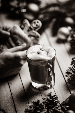 Photo of the female hand holding man shaped cookie in a sock and cup of coffee lying on the Christmas decorations backgroundの写真素材