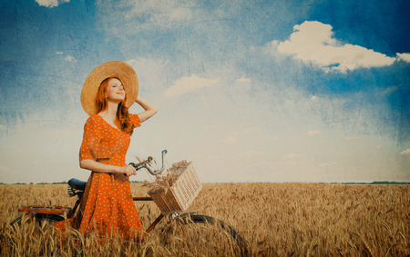 Redhead peasant girl with bicycle on wheat field.の写真素材