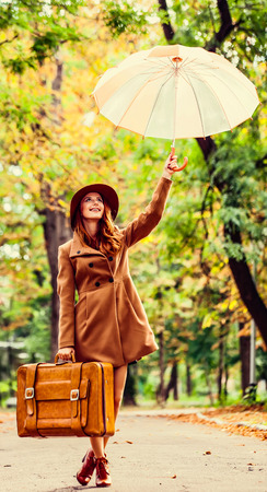 Redhead girl with umbrella and suitcase in the autumn park.の写真素材
