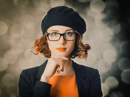 portrait of a beautiful girl with curly hair dressed in a beret and jacket against a gray...