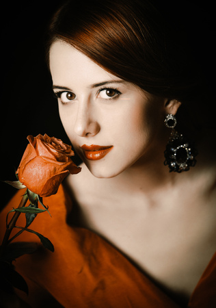 Portrait of a beautiful girl in a red dress holding a red rose near the face.の写真素材