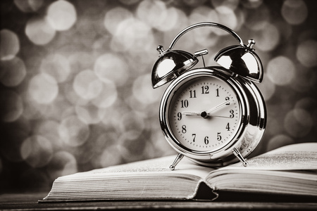 Metal alarm clock and open book. Photo in black and white color image style.の写真素材