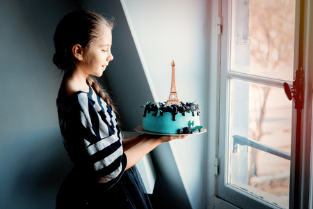 Young girl holding a cream cake with Eiffel tower on it near windowの写真素材