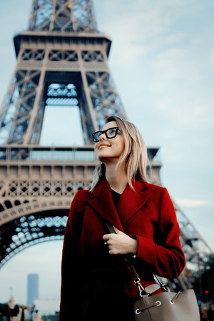 Style redhead girl in red coat and bag at parisian street with view at Eiffel tower in autumn season timeの写真素材