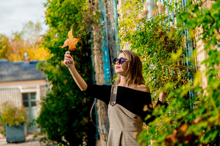 Young girl in sunglasses holding a leaf in hands and looking on it. Autumn season timeの写真素材