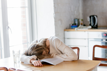 Tired caucasian girl in white sweater with book at kitchen. Home locationの写真素材