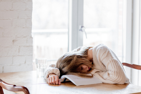 Tired caucasian girl in white sweater with book at kitchen. Home locationの写真素材