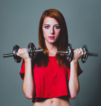 Sport woman in red shirt with dumbbells on gray backgroundの写真素材