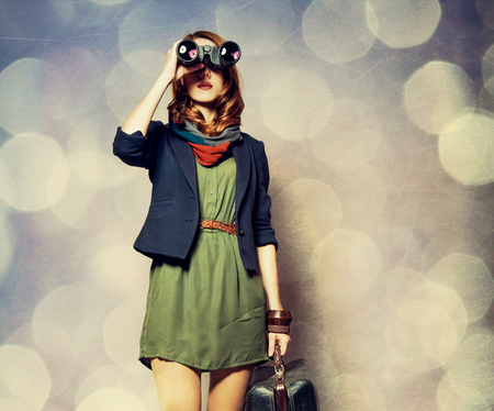 Style redhead girl with binocular and suitcase on ray background with bokehの写真素材
