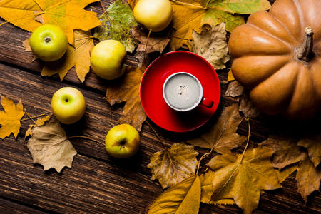 photo of the fallen leaves, pumpkin, apples and red cup of coffee on the brown wooden backgroundの写真素材