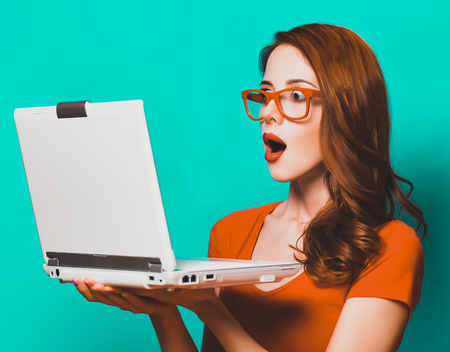 Redhead girl with laptop on blue background.の写真素材