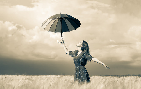 a young girl is standing on a wheat field with umbrella and waiting for rain. Image in old sepia styleの写真素材