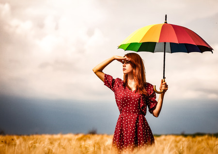 a young girl is standing on a wheat field with umbrella and waiting for rain.の写真素材