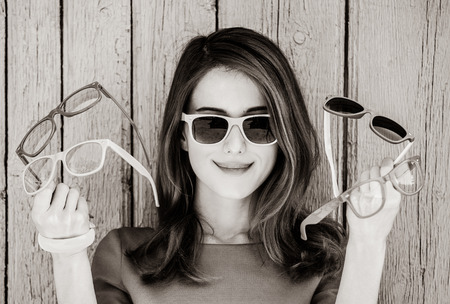 Style adult girl with collection of sunglasses on wooden background. Image in black and white color