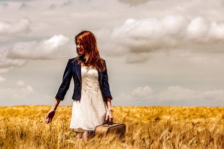 Young girl in white dress and black jacket with suitcase stay at wheat field.の写真素材
