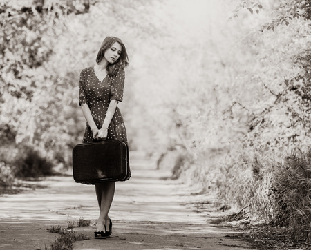 Style cuacasian adult girl in dress with travel suitcase staying on rural road. Image in black and white color styleの写真素材