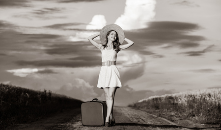 Beautiful redhead girl in white dress with suitcase at rural road. Image in black ahd white color styleの写真素材