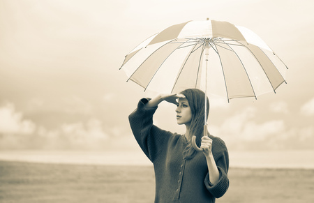 Beautiful adult girl in sweater with umbrella at wheat field and cloudscape on background. Image in sepia color styleの写真素材