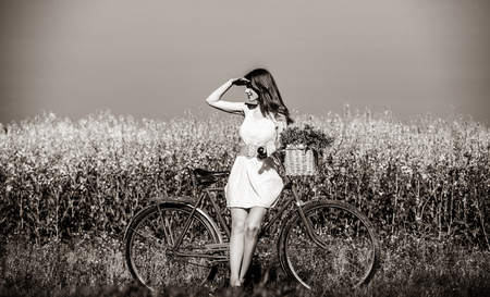 Beautiful girl in white dress with bike and flowers at wheat filed at countryside. Image in black and white color styleの写真素材