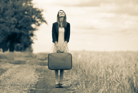 Young beautiful adult girl with suitcase on rural road during travelling. Image in black and white color styleの写真素材