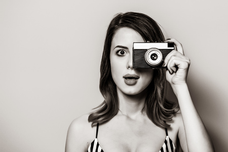 Portrait of beautiful young surprised white woman in striped dress with retro camera. Image in black and white color style.の写真素材