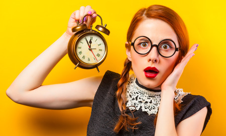 girl in glasses with two pigtails holding classic alarm clock on yellow backgroundの写真素材