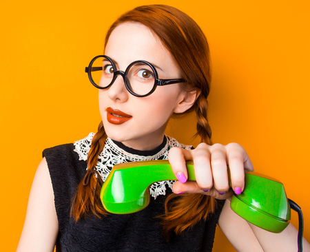 surprised young girl in glasses with two pigtails holding handset on yellow backgroundの写真素材