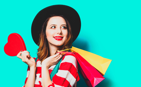 Portrait of young smiling red-haired white european woman in hat and red striped shirt with heart...