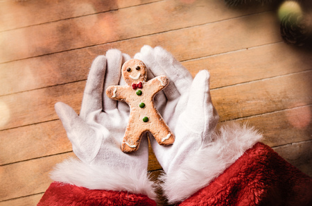 Santa Claus holding Chrstmas cookie on wooden background with bokehの写真素材