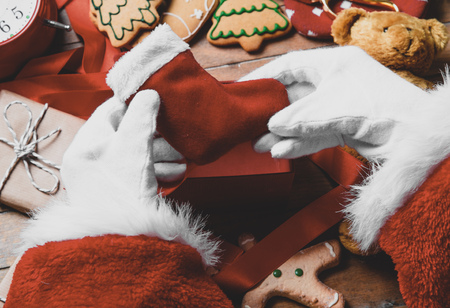 Santa Claus have wrapping a Christmas sock and other gifts on wooden background