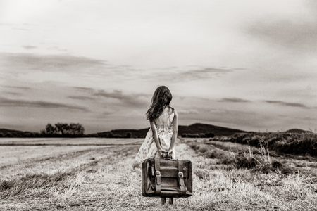 Little girl in classic dress with travel suitcase at autumn wheat field. Tourist concept image . Image in black and white color styleの写真素材