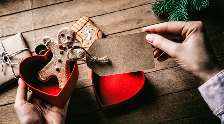 Young woman's hands holding Christmas gingerbread man cookie with tag on wooden background, Photo in old color image styleの写真素材